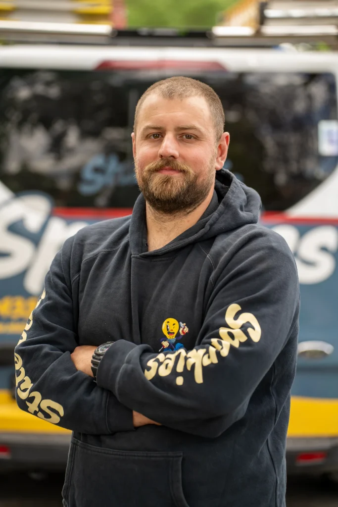 Statewide Sparkies electrician in branded hoodie standing with arms crossed in front of a company service van