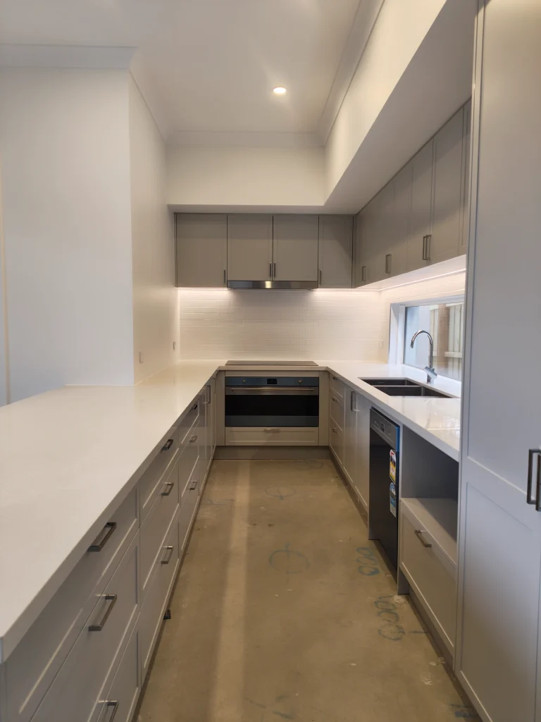 Newly renovated kitchen with grey cabinetry, white stone benchtops, built-in oven, rangehood and recessed downlights installed by Statewide Sparkies