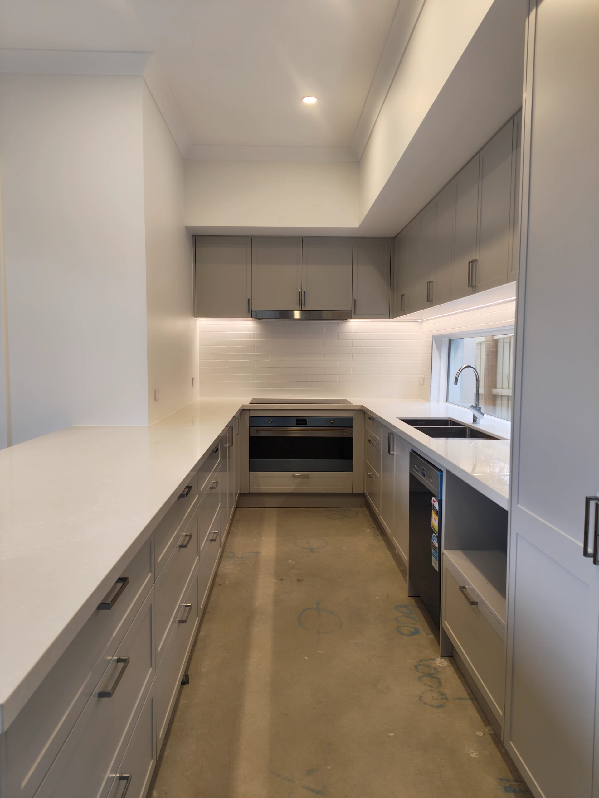 Newly renovated kitchen with grey cabinetry, white stone benchtops, built-in oven, rangehood and recessed downlights installed by Statewide Sparkies