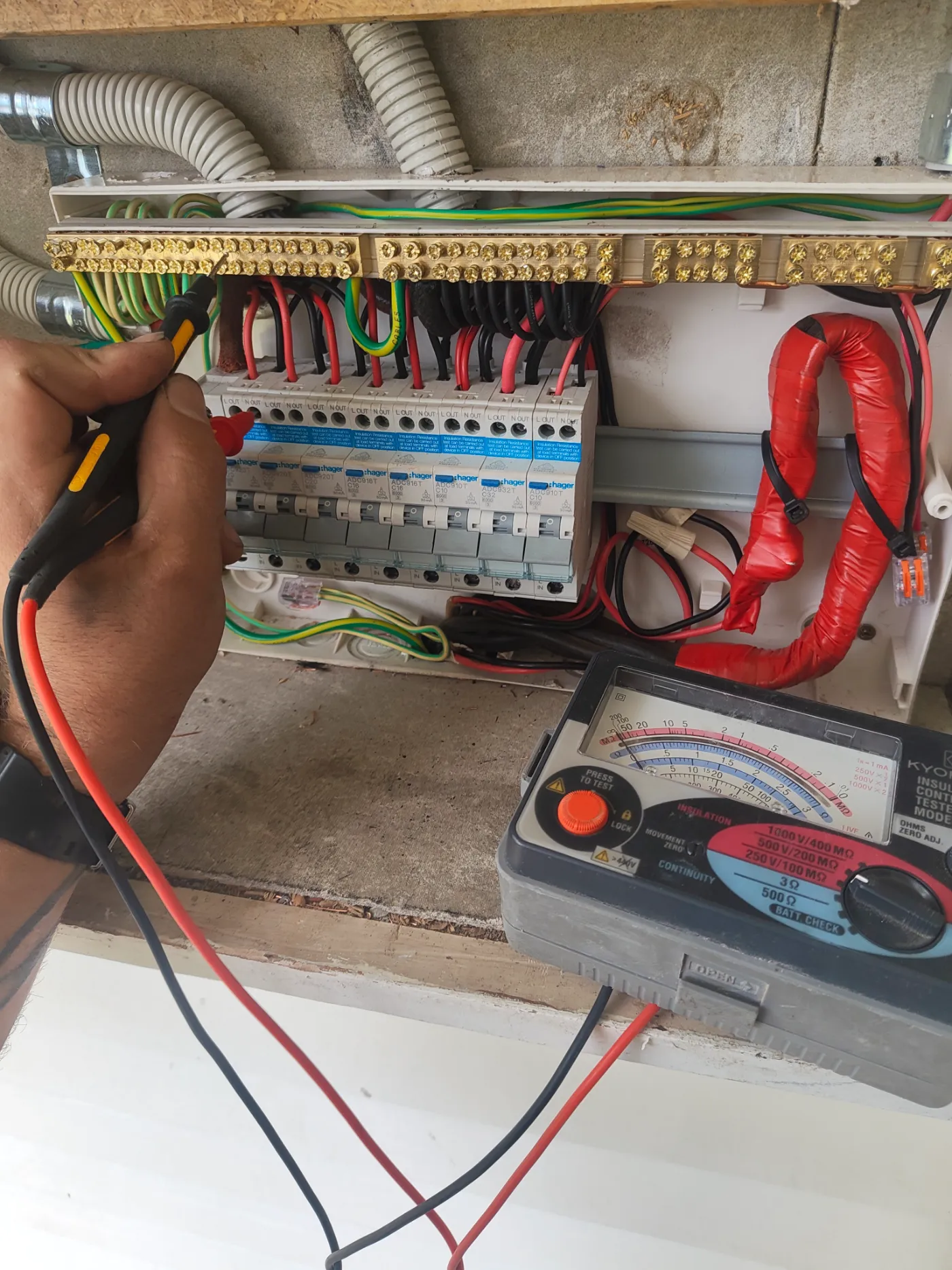 Electrician testing a switchboard with an insulation resistance tester and probe during an electrical fault diagnosis
