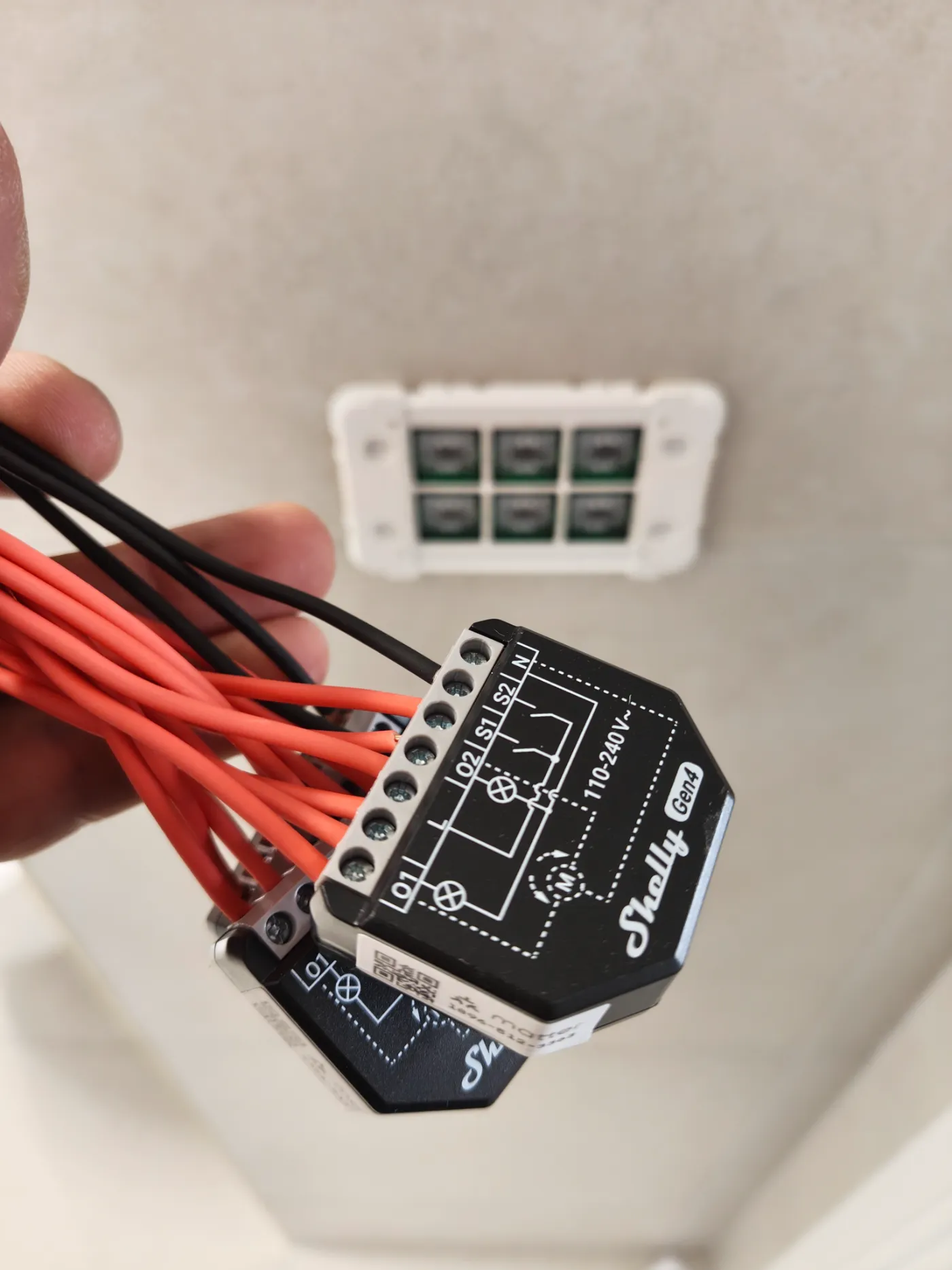 Electrician holding Shelly smart relay modules with wiring during a home automation installation, with a smart wall switch in the background