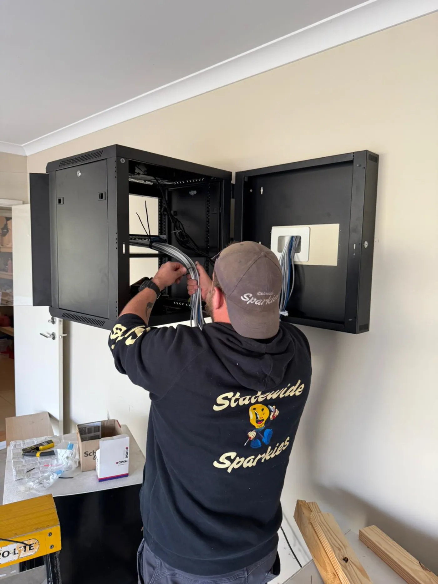 Statewide Sparkies electrician installing a wall-mounted network cabinet with data cabling inside a residential home
