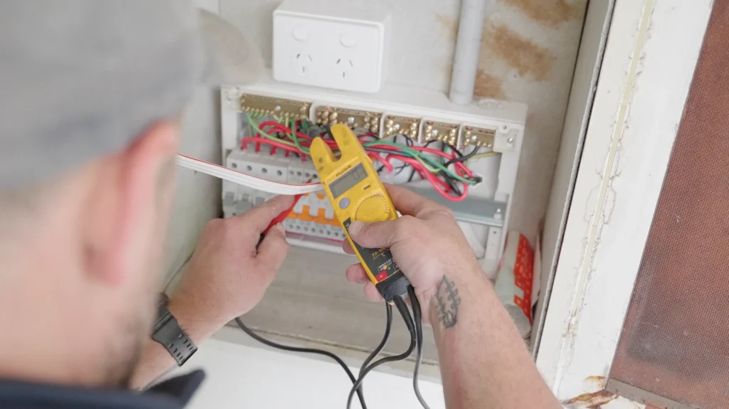 Electrician performing an electrical safety check using a voltage tester on an open switchboard at a residential property